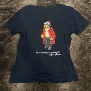 Mörkblå Polo Bear t-shirt Ralph Lauren - Snygg mörkblå t-shirt från Ralph Lauren med ikoniska Polo Bear-trycket på bröstet. Björnen har röd jacka, stickad tröja och rutiga byxor. Klassisk passform och rund hals. Perfekt för dig som gillar streetstyle och vill sticka ut lite extra. Storleken är medium i barnstorlek så ungefär 12 år! Kom med bud eller frågor.