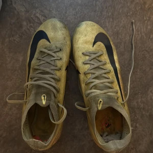 Gula Nike fotbollsskor med svarta detaljer smutsiga men är väldigt sköna skor modell är PRO och är i storlek 42,5  - Säljer ett par gula Nike fotbollsskor med svarta swoosh-loggor på sidorna och orange dobbar undertill. Skorna har snörning och är tillverkade i syntetmaterial. Perfekta för dig som vill sticka ut på planen med en sportig look.