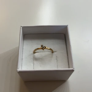 Guldfärgad ring med fjäril och stenar - Söt guldfärgad ring med en liten fjäril dekorerad med glittrande stenar. Ringen är tunn och elegant, perfekt för dig som gillar detaljer med lite extra bling. Fjärilen ger en trendig och lekfull touch till din stil.