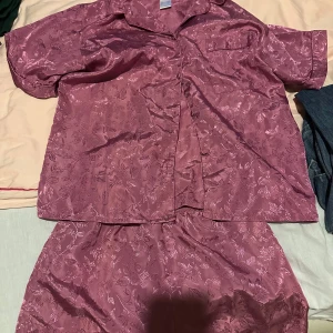 blommigt pyjamas set i rosa - snyggt pyjamasset glansigt satinmaterial med blommigt mönster. Settet har ett avslappnad passform och elastisk midja för extra komfort. Perfekta för mysiga hemmakvällar eller när du vill känna dig extra lyxig.