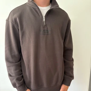 Brun half zip sweatshirt från H&M - Mörkbrun sweatshirt från H&M med halv dragkedja och tryck på bröstet. Skön, stilren och snygg. 
