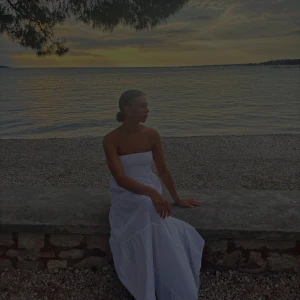 Vit axelbandslös långklänning - Superfin vit långklänning med axelbandslös design och smockad överdel. Klänningen är pyttelite genomskinlig och användes endast en gång 