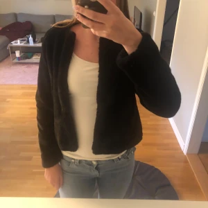 Svart pälsjacka  - Mysig svart pälsjacka med lång ärm. Jackan är croppad och har en stilren look som passar perfekt till allt. Materialet är mjukt och fluffigt, vilket ger en lyxig känsla. Enkel att matcha och perfekt för kyligare dagar. Jackan är super len!! Säljer den då den är lite för liten och kommer ej till användning! Har använt den 1 gång! Man kan stänga jackan med spännen som fungerar typ som knappar!
