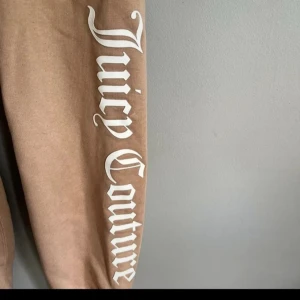 Beige Juicy Couture mjukisbyxor XS - Beiga mjukisbyxor från Juicy Couture med stort vitt tryck längs ena benet. Byxorna har resår och snörning i midjan, två fickor fram och muddar vid bensluten. Perfekta för chill dagar eller när du vill ha en avslappnad look. Byxorna är i fint skick.