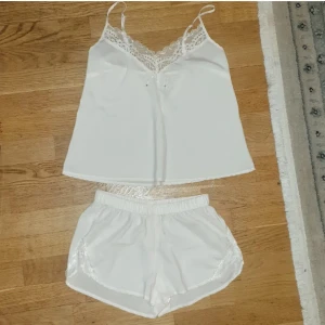 Vit linnetopp & shorts med spetsdetaljer - Säljer en söt vit linnetopp med tunna axelband och v-ringning dekorerad med spets. Toppen är i ett mjukt, lätt material och har en feminin känsla med spetsdetaljer både fram och längs kanterna. Tillhörande shorts.