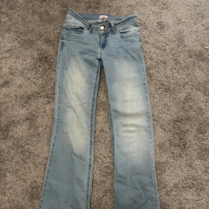 Ljusblå bootcut jeans från Nelly - Säljer ett par väldigt populära ljusblå bootcut jeans från Nelly med dubbla knappar i midjan. Jeansen har en snygg tvätt och är tillverkade i mjukt bomullsmaterial med lite stretch. En liten defekt ser ni på sista bilden! Använda fåtal gånger