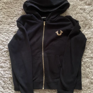 Svart hoodie True Religion med guldtryck - Svart hoodie från True Religion med guldfärgat tryck på bröstet och ryggen. inga tecken på användning. står storlek M men skulle mer säga att den sitter som S. skriv för fler bilder eller frågor💕