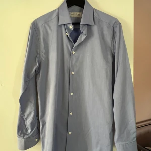 Ljusblå skjorta från These Glory Days - Klassisk ljusblå skjorta från These Glory Days med snygg krage och vita knappar. Skjortan är långärmad och har en stilren, enkel design som passar perfekt till jeans eller chinos. Tillverkad i mjuk bomull för en bekväm känsla hela dagen.