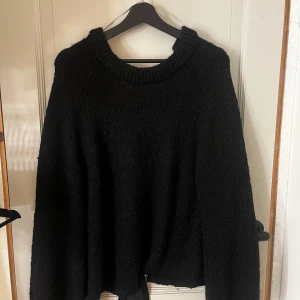 Svart stickad tröja med rosett i ryggen - Svart stickad tröja från Arket med bred ribbad halsringning och lång ärm. Baksidan har en snygg öppen detalj med en stor rosett i satinliknande tyg som knyts i nacken. Perfekt för dig som vill ha en basic tröja med en twist.