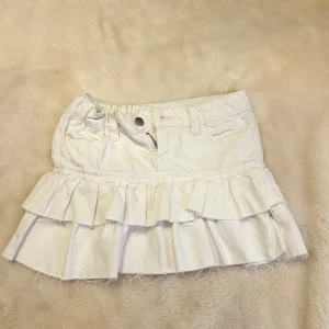 Vit volangkjol från Gina Tricot - Supersöt vit kortkjol från Gina Tricot med dubbla volanger och råa kanter. Kjolen är justerbar, och passar mig som brukar ha xxs trots att den är i storlek 146💞