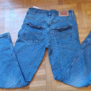 Levi's 501 blå jeans 158-164 - Klassiska Levi's 501 jeans i blå denim med raka ben och femficksmodell. Snyggt slitna detaljer framtill och ikonisk läderpatch bak i midjan. Perfekta för dig som gillar tidlös stil och vill ha ett par jeans som funkar till allt. Har en slitning i bakfickan