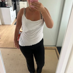 Vit linnetopp med draperad front - Säljer en vit linnetopp med smala axelband och snyggt draperad front. Toppen har en lätt vågig nederkant och är tillverkad i ett tunt, mjukt material som känns luftigt. Perfekt för dig som gillar en enkel men ändå trendig look.