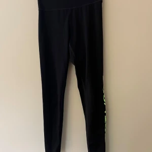 Svarta sportleggings från H&M - Svarta sportiga leggings från H&M med neongrön text 'SPORT MODE' längs ena benet och neongrönt foder i midjan. Tight passform och stretchigt material som passar perfekt till träning eller chill. Snygg och bekväm design för dig som gillar att sticka ut.
