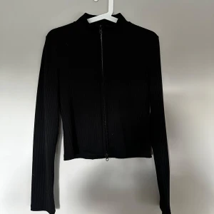 Svart ribbad kofta från Vero Moda - svart ribbad tröja från Vero Moda i storlek M med dragkedja framtill. 