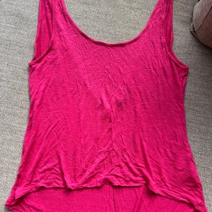 Cerise linnetopp från Bik Bok - Säljer en snygg ceriserosa linnetopp från Bik Bok i 100% viskos. Toppen har rundad ringning fram och djup v-ringning bak, är ärmlös och har en lite längre bakdel för en cool look. Perfekt för varma dagar eller att styla lager på lager.