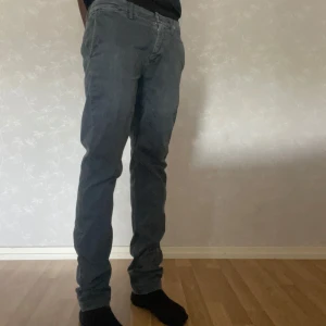 Gråa chinos från Replay, modell Benni - Snygga grå chinos från Replay, modell Benni. Byxorna har raka ben, bälteshällor och två bakfickor med diskreta ficklock. Tillverkade i mjuk bomullsmix som ger en skön känsla och stilren look. Perfekta för dig som gillar en clean och avslappnad stil.