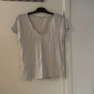 Ljusgrå basic t-shirt med v-ringning - Enkel och stilren ljusgrå t-shirt med djup v-ringning och korta ärmar. Tillverkad i mjuk bomull som känns skön mot huden. Perfekt för en avslappnad look och lätt att matcha med allt i garderoben. OBS något genomskinlig 