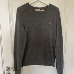 Grå Kashmir från Lacoste - Mjuk och stilren grå tröja från Lacoste i 100% kashmir med diskret krokodillogga på bröstet. Klassisk rund halsringning och långa ärmar. Perfekt för dig som gillar en clean och enkel look med premiumkänsla. Nypris 1599