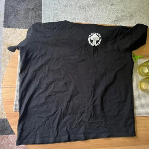 Svart Zubbis t-shirt med svamptryck - Svart t-shirt från Zubbis med stort färgglatt tryck på ryggen med svampar och texten 'Original Dunder Zubbis' i orange. Mindre logga framtill. Klassisk passform och rund hals. Perfekt statement-plagg för dig som gillar unika prints.
