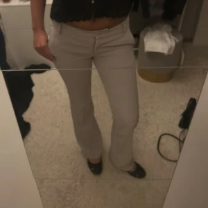 Vera Kostymbyxor - Snygga beiga kostymbyxor med bootcut-snitt och klassisk passform. Byxorna har fickor fram och bälteshällor i midjan. Perfekta för en clean och stilren look.