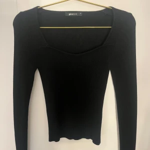 Svart ribbad topp från Gina Tricot - Svart långärmad topp i storlek xs från Gina Tricot i ribbat material. Toppen har en snygg u-ringad halsringning och sitter tight mot kroppen. Perfekt att styla med jeans eller kjol för en clean look.