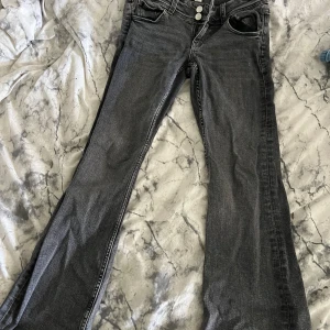 Grå bootcut jeans från Gina Tricot - Snygga grå jeans från Gina Tricot i bootcut-modell med två knappar och dragkedja framtill. 