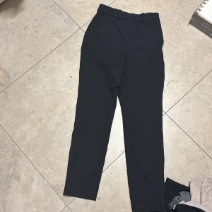 Svarta kostymbyxor från H&M - Svarta kostymbyxor från H&M i storlek 34. Byxorna har diskreta tunna ränder, hällor för bälte och två bakfickor. Klassisk rak passform och midja. Perfekta för en clean och stilren look.