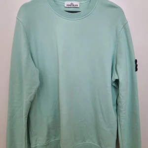 Mintgrön sweatshirt från Stone Island - Fräsch mintgrön sweatshirt från Stone Island med klassisk logga på ärmen. Tröjan har rund halsringning och långa ärmar. Tillverkad i mjuk bomull som är skön att bära. Perfekt för dig som gillar stilrena och cleana plagg med streetkänsla.