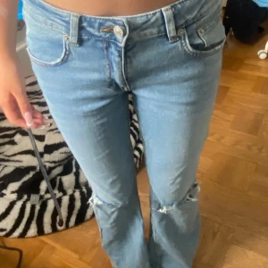 Ljusblå bootcut jeans från 157 - Säljer ett par ljusblå jeans från 157 med bootcut passform och slitna hål vid knäna. Jeansen har klassisk femficksdesign, normalhög midja och är tillverkade i mjukt bomullsjeans. Perfekta för en avslappnad och trendig look.