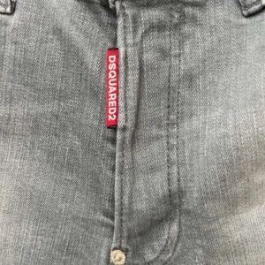 Grå Dsquared2 jeans - Säljer ett par grå skinny jeans från Dsquared2 med slitna detaljer och ljusa partier på benen. Jeansen har klassisk femficksdesign, dragkedjegylf och röd Dsquared2-tag vid fickan. Perfekta för dig som gillar en edgy streetstil.