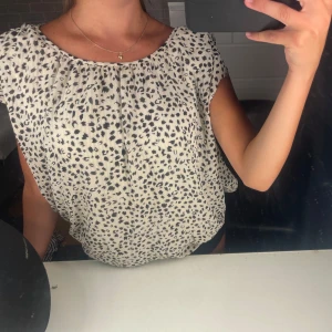 Vit blus med svart leopardmönster från kapphal  - Säljer en fin luftig vit blus med svart leopardmönster. Blusen har rund halsringning och ärmlös design med lätt rynk vid halsen. Skriv för fler frågor!