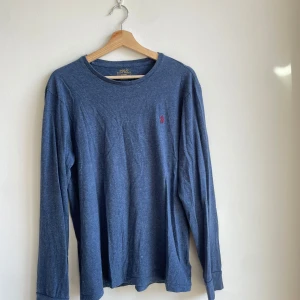 Blå långärmad tröja Polo Ralph Lauren - Säljer en blå långärmad tröja från Polo Ralph Lauren i bomull. Tröjan har en relaxed passform och klassisk rund halsringning. På bröstet finns det ikoniska röda broderade Polo-loggan. Perfekt för dig som gillar stilren och enkel design.