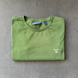 Grön t-shirt från GANT i bomull - Snygg grön t-shirt från GANT med klassisk rund hals och diskret broderad logga på bröstet. Tillverkad i mjuk bomull som känns skön mot huden. Enkel och stilren design som passar perfekt till jeans eller shorts. PRISET ÄR FÖRHANDLINGSBART!! 