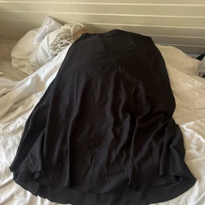 Svart långkjol från The Black Label - Svart långkjol från The Black Label Collection i flowigt tyg. Kjolen har en enkel och stilren design med lätt vidd nertill och resår i midjan för skön passform. Perfekt för dig som gillar minimalistisk och tidlös stil.