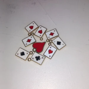 Pokerinspirerade berlocker i emalj - Flera små berlocker i form av spelkort med essmotiv, i färgerna rött, svart och vitt. Berlockerna har guldfärgade kanter och är perfekta att använda till halsband, armband eller örhängen för en unik och lekfull stil.