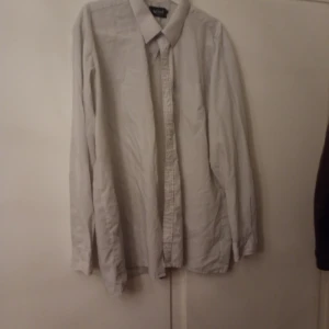 Ljusgrå skjorta med knappar - En stilren ljusgrå skjorta med klassisk krage och knäppning framtill. Skjortan har långa ärmar och en enkel, tidlös design som passar till många olika outfits. Perfekt för dig som gillar en clean och minimalistisk look.