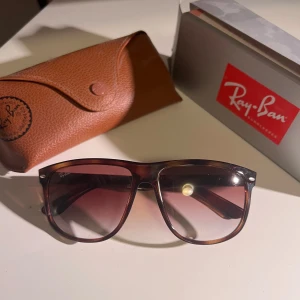 Ray-Ban boyfriend  - Snygga solglasögon från Ray-Ban med brun plastbåge och tonade glas. Modellen har en klassisk, lite större fyrkantig form och kommer med original Ray-Ban fodral i brunt läder. Perfekta för att lyfta din stil i solen. Glasögon är självklart äkta och köptes in förra sommaren och har knappt används, kvitto finns. Kan gå ner i pris vid snabb affären. Allt og följer med.
