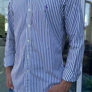 Ralph lauren skjorta strl M - Snygg skjorta från Ralph Lauren med svarta och vita vertikala ränder och klassisk krage.          Skick 9/10🤩|Fraltar inom 48h📦|hör av dig vid minsta lila fundering!