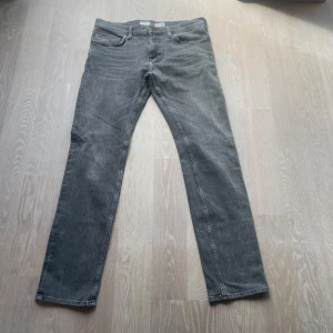 Gråa Tommy Hilfiger jeans, semi fit - Säljer ett par gråa jeans från Tommy Hilfiger i semi fit-modell. Jeansen har klassisk femficksdesign, diskret stretch och snygga slitningar för en avslappnad look. Liten Hilfiger-flagga på bakfickan och läderpatch i midjan.