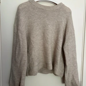 Beige stickad tröja från Gina Tricot - Mysig beige stickad tröja från Gina Tricot med ribbade muddar vid ärmslut och nederkant. Tröjan har en avslappnad passform och rund halsringning, perfekt för lager-på-lager under kyliga dagar. Den är i fint skick men finns tecken på användning.