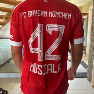 Bayern München Musiala #42 matchtröja - Säljer en röd och vit Bayern München fotbollströja från Adidas med Musiala #42 på ryggen. Urtjusig tröja med Musiala på, helt oanvänd. Skön kvalité, tröjan är köpt utomlands 