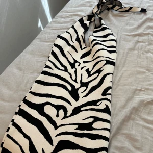 Zebramönstrad halterneck klänning - Snygg kort zebramönstrad klänning med halterneck och knyt i nacken. Klänningen har svartvitt mönster och är figurnära med en cool 90-talsvibe. Perfekt för dig som vill sticka ut med en trendig look.