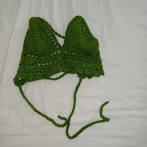 Grön virkad croppad linnetopp - Säljer en handvirkad grön linnetopp med snörning i ryggen och fina virkade detaljer längs nederkanten. Toppen är croppad och har trekantsformade kupor, perfekt för sommarens varma dagar. Supersöt och unik stil!