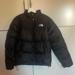 Svart saikuru vinterjacka från The North Face - Säljer en svart pufferjacka (saikuru) från The North Face i storlek S. Jackan har hög krage utan luva, dragkedja framtill, två sidofickor och en innerficka. Alla fickor har dragkedja och är fodrade med fleecetyg. Klassisk logga på bröstet och baksidan. Perfekt för kalla dagar. Använd ett fåtal gånger.