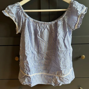 Blårandig blus med spetsdetaljer - Söt blårandig blus med korta ärmar och offshoulder-modell. Vet tyvärr inte märket då det inte står nått och inte storlek heller.. finns ingen lapp! Skulle säga det är S