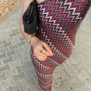 Mönstrad oneshoulder långklänning - Säljer en lång, figurnära oneshoulder-klänning med snyggt zickzackmönster i vinrött, svart och vitt. Klänningen har en cool asymmetrisk axel och är perfekt för dig som vill sticka ut. Materialet känns mjukt och följsamt mot kroppen.