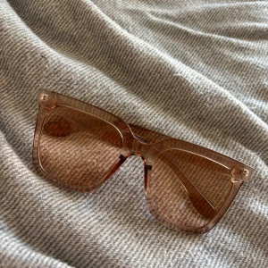 Bruna/oranga transparenta solglasögon - Säljer ett par trendiga solglasögon med transparent brun båge och stora fyrkantiga glas. Snygg och modern design som ger en cool vibe till din outfit. Perfekta för att lyfta din stil under soliga dagar.