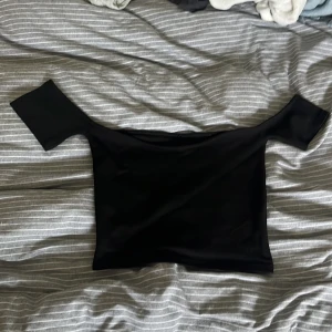 Svart offshoulder croppad topp - Snygg svart offshoulder topp med croppad passform. Toppens axelbandslösa design ger en clean och modern look, perfekt att styla med höga jeans eller kjol. Gjord i stretchigt material som sitter bekvämt och följer kroppen. Köpt second hand i fint skick och aldrig använd efter det🩷lappen på ryggen är avklippten skulle gissa storlek S