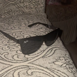 Svarta solglasögon från Ray-Ban - Snygga svarta solglasögon från Ray-Ban med klassisk rektangulär form och diskret logga på bågen. Bågarna är i svart plast med stilrena detaljer och mörka glas. Perfekta för att ge din look en cool vibe.