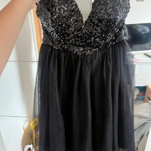 Svart glittrig kort klänning - Supersnygg svart kort klänning med glittrig paljett-topp och v-ringning. Aldrig använd 
